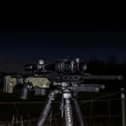 IRay Mate MAH50 | 50mm Clip-On Thermal W/ 2400 Yard Range 32 IRay Mate MAH50 | 50mm Clip-On Thermal W/ 2400 Yard Range -Tactical Equipment gallery image quarter angle shot of high precision rifle equipped with iray mate mah50 mounted on sturdy tripod against a nighttime backdrop